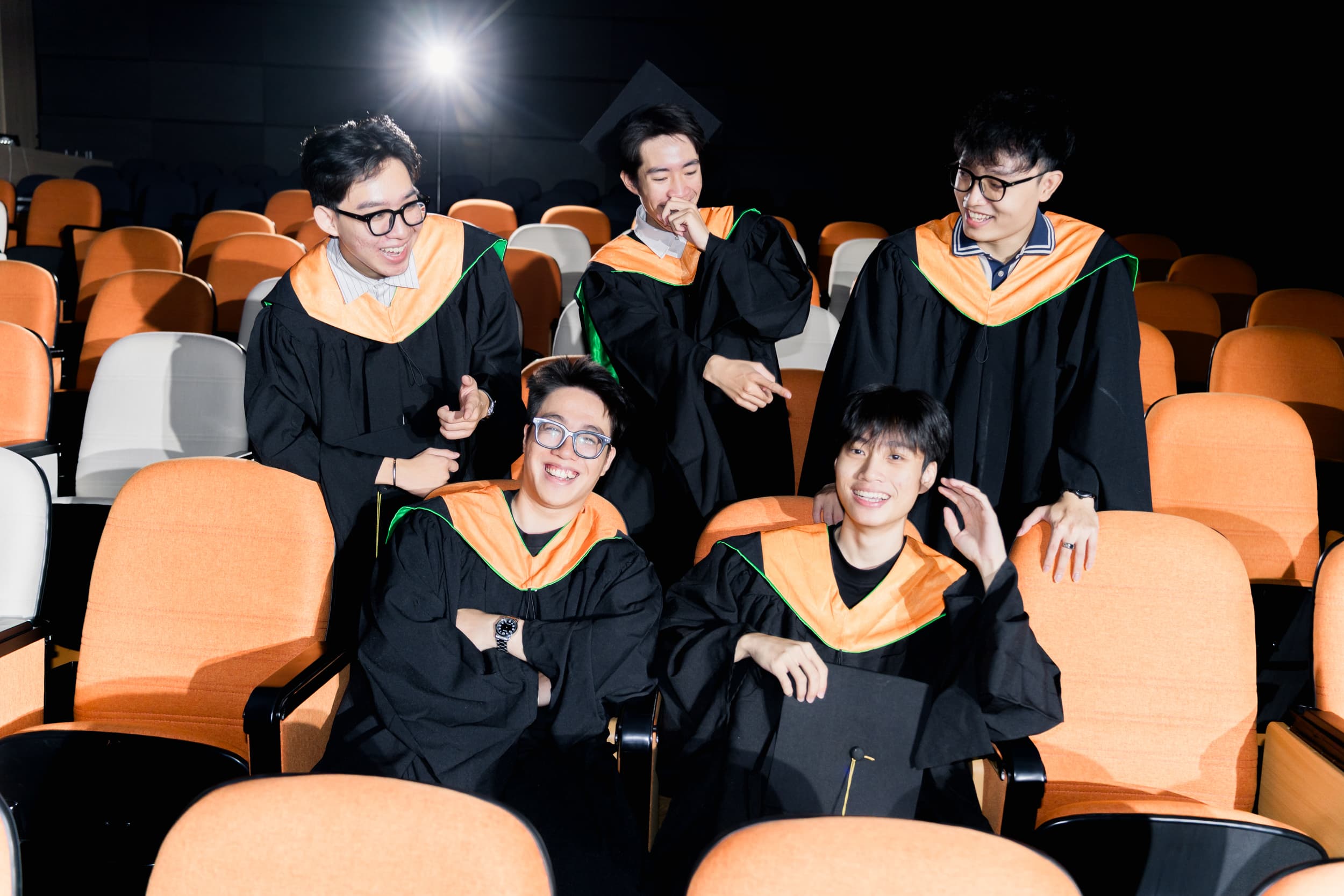 Five graduates sharing a joyful moment in the auditorium