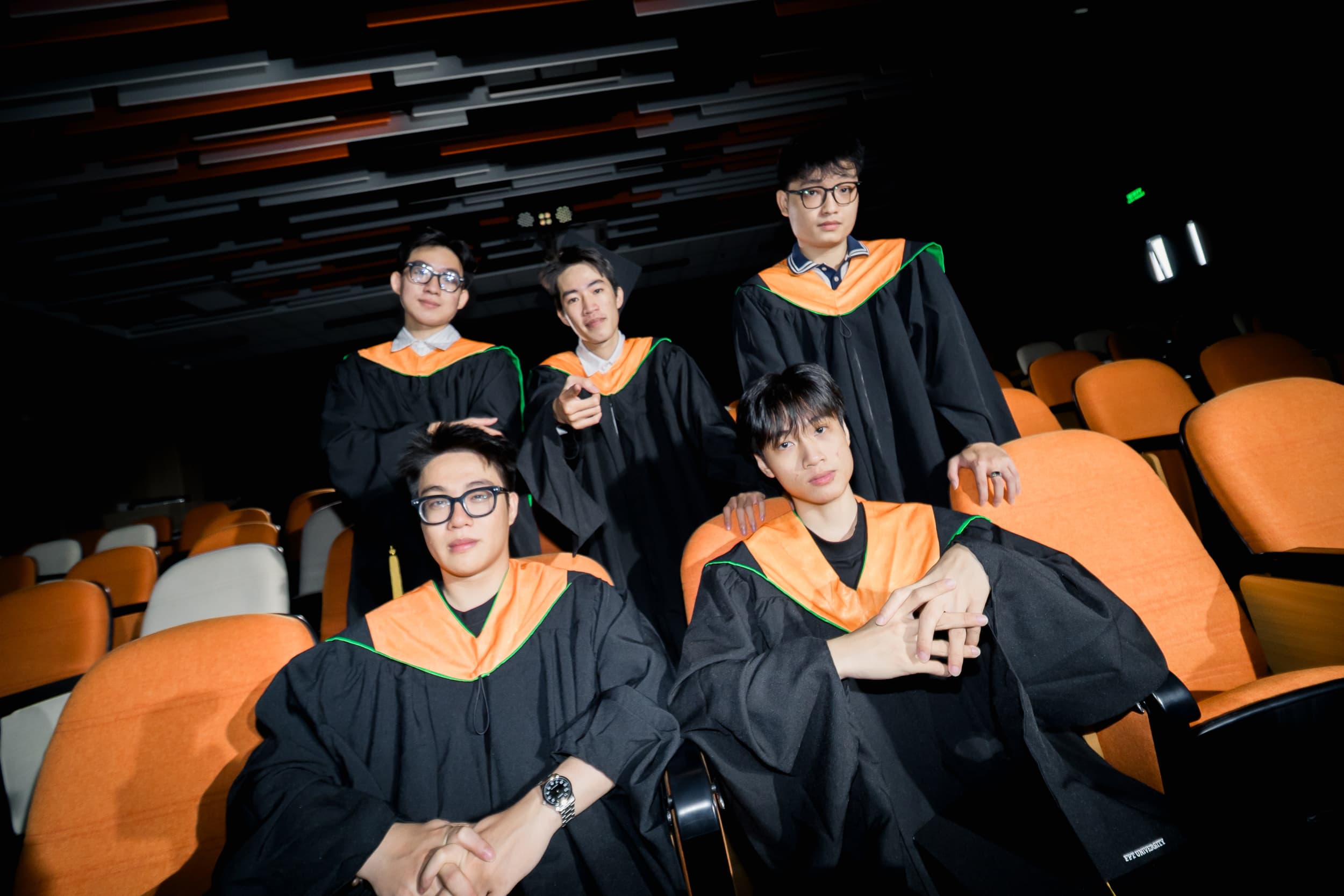 Five graduates posing together among auditorium seats