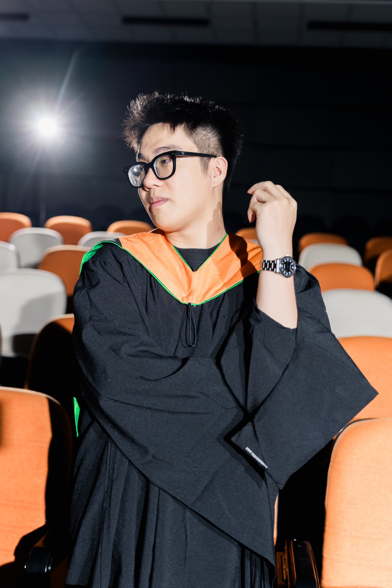 Graduate seated among the auditorium seats in a thoughtful pose