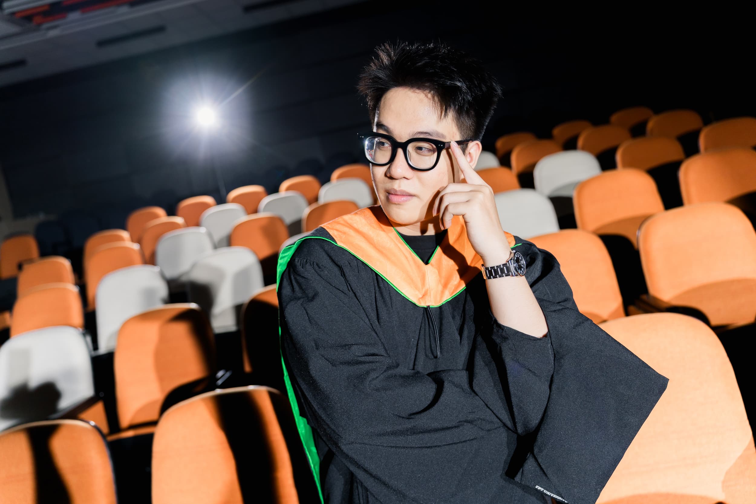 Graduate seated among the auditorium seats in a thoughtful pose